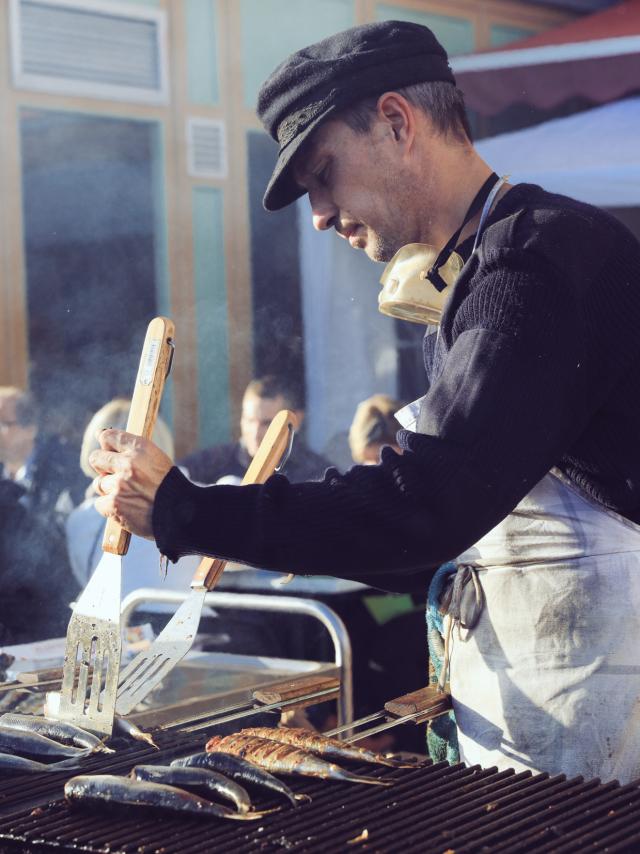 Un homme retourne des harengs sur un grill à l'aide de spatules