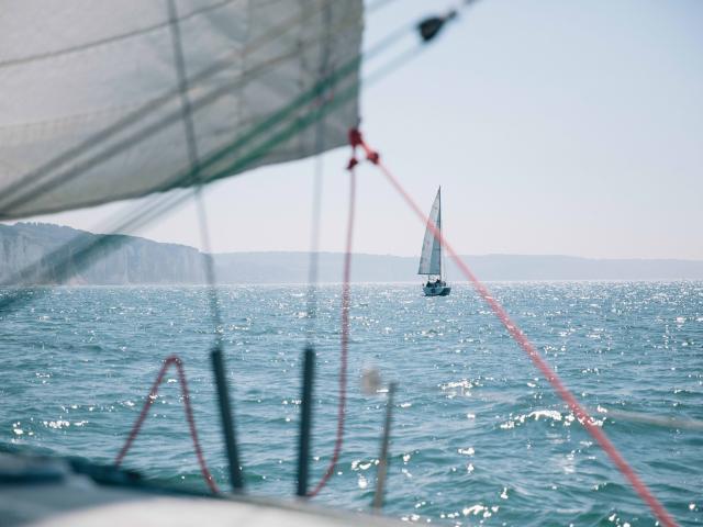 Depuis un voilier, vue sur un autre voilier au large et sur les falaises en arrière plan