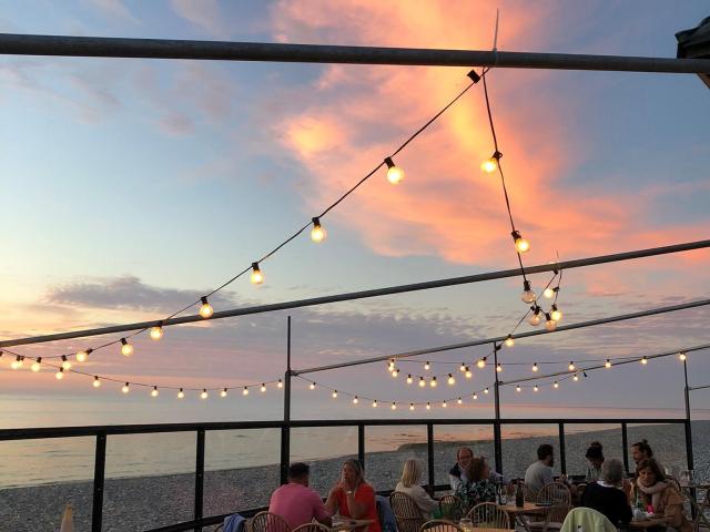 Terrasse d'un bar-restaurant sur les galets illuminée de guirlandes guinguettes à la lumière du soir