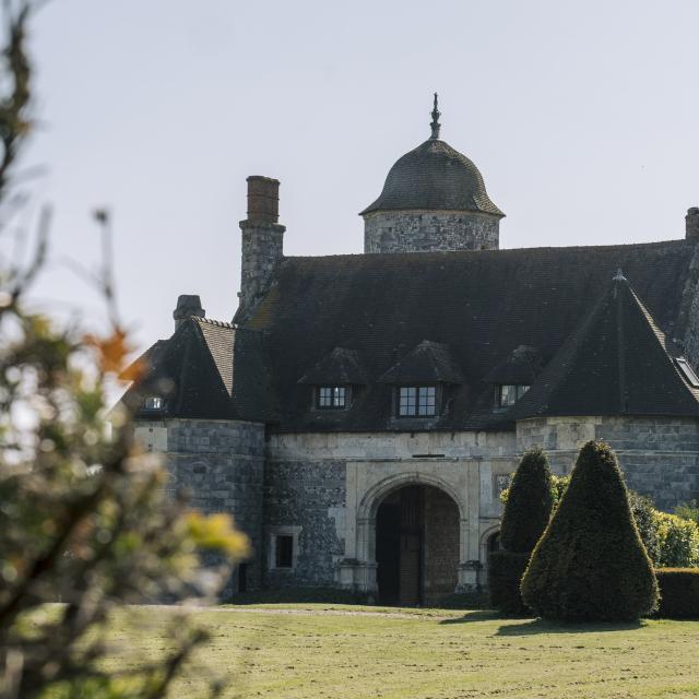 Un manoir de style renaissance en vieilles pierres avec une allée bordée de topiaires