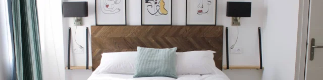 Chambre d'hôtel lumineuse et raffinée avec un lit double au linge de lit blanc, une tête de lit en bois, des tableaux modernes