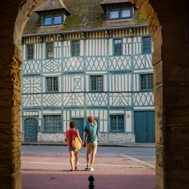 Deux visiteurs découvrent la Maison Miffant à Dieppe, remarquable façade à pans de bois, vue sous une arche en pierre.