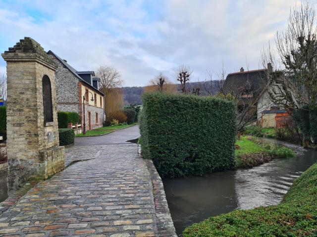 Scène hivernale d'un petit pont en pierre au-dessus d'une rivière dans un village bucolique en bordure de forêt