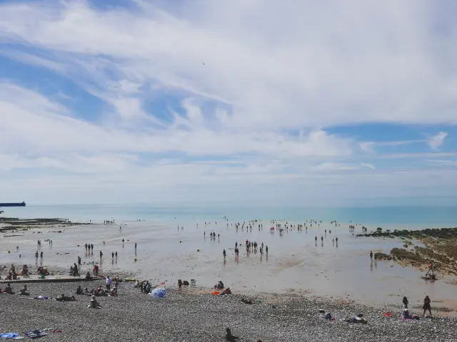 Vue d'ensemble de la plage de Puys où on voit sur les extrémités les différents rochets et au centre une foule de personnes allant ou revenant de la baignade