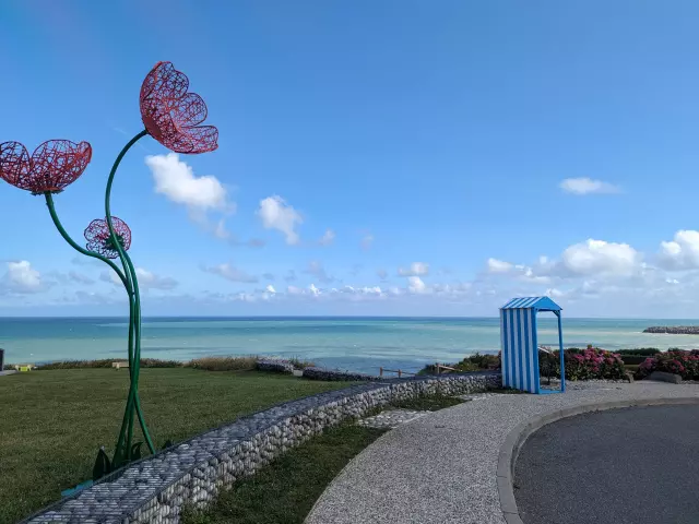 Photographie de la mer de Petit-Caux avec au premier plan une plante en métal qui décore le parking.