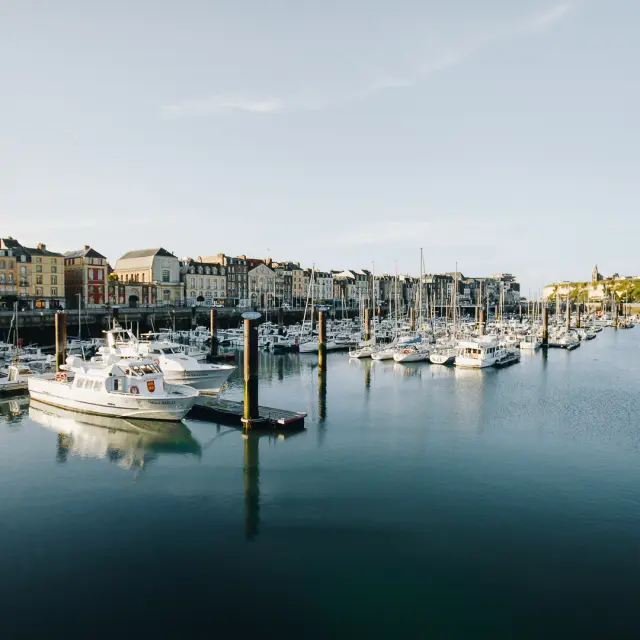 Vue du port de plaisance de Dieppe bordé de façades colorées, avec ses voiliers amarrés dans une eau calme sous un ciel dégagé.