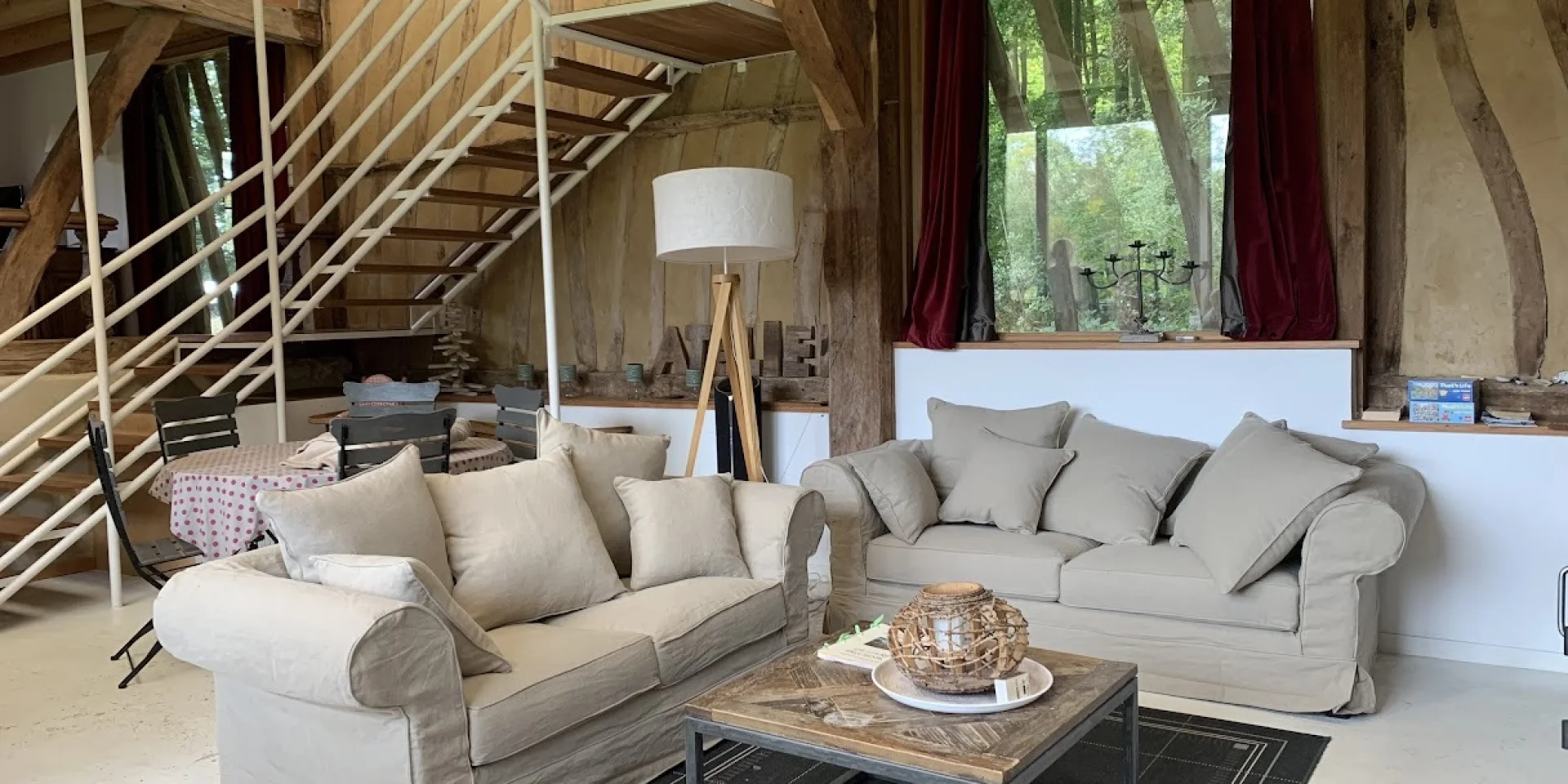 Un coin séjour chaleureux dans un gîte de charme orné de poutres en vois et d'un escalier style industriel
