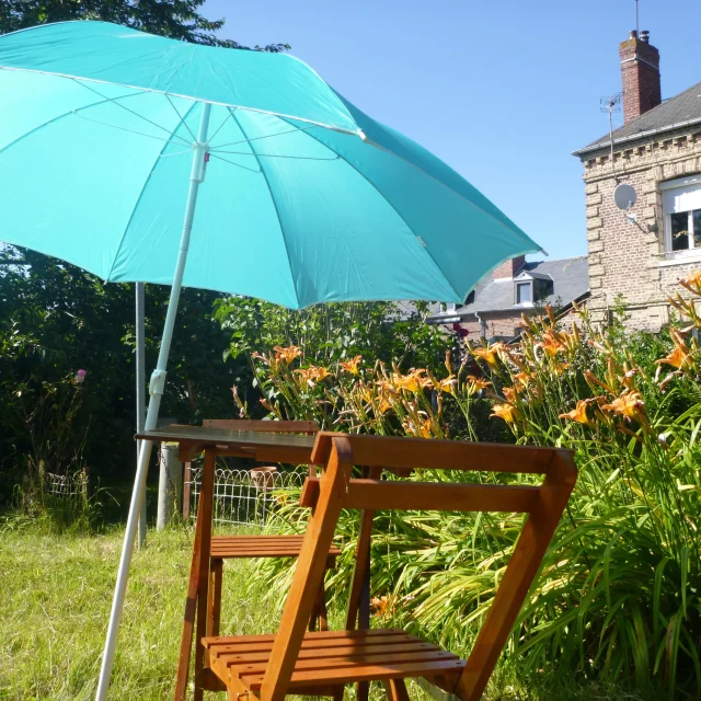Un petit salon de jardin, dans un jardin arboré et fleuri, devant une maison en briques
