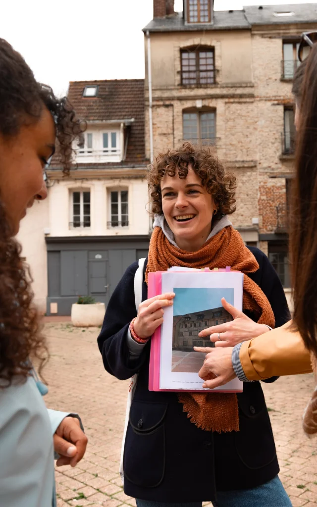 Une guide souriante montre une photo d’archive à deux participantes lors d’une visite commentée dans le centre historique de Dieppe.