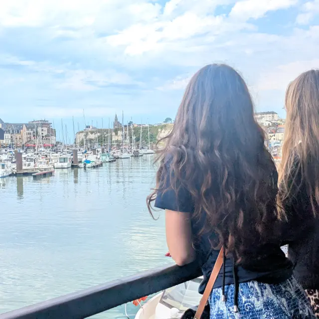 Visiteurs admirant le port de plaisance de Dieppe depuis une terrasse, face aux voiliers amarrés et à la chapelle Notre-Dame-de-Bonsecours sur les falaises.