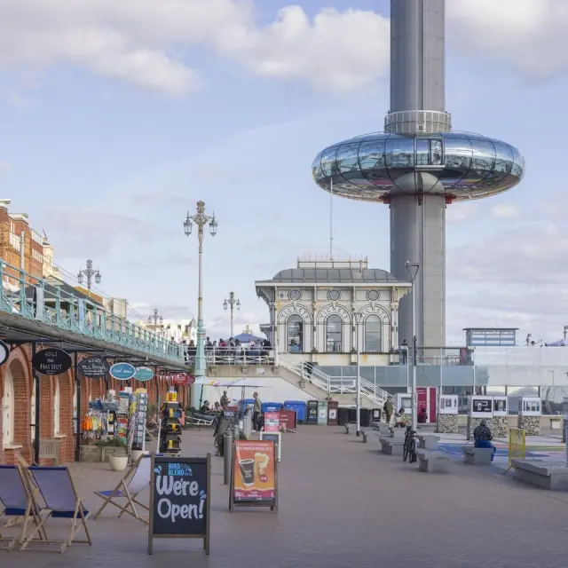 Promenade du front de mer de Brighton bordée de commerces et de terrasses, avec la tour d’observation i360 en arrière-plan.