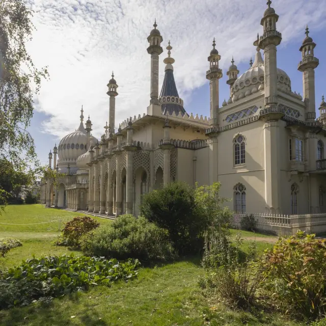 Royal Pavilion de Brighton vu depuis ses jardins, avec ses dômes, minarets et façades d’inspiration orientale entourés de verdure.