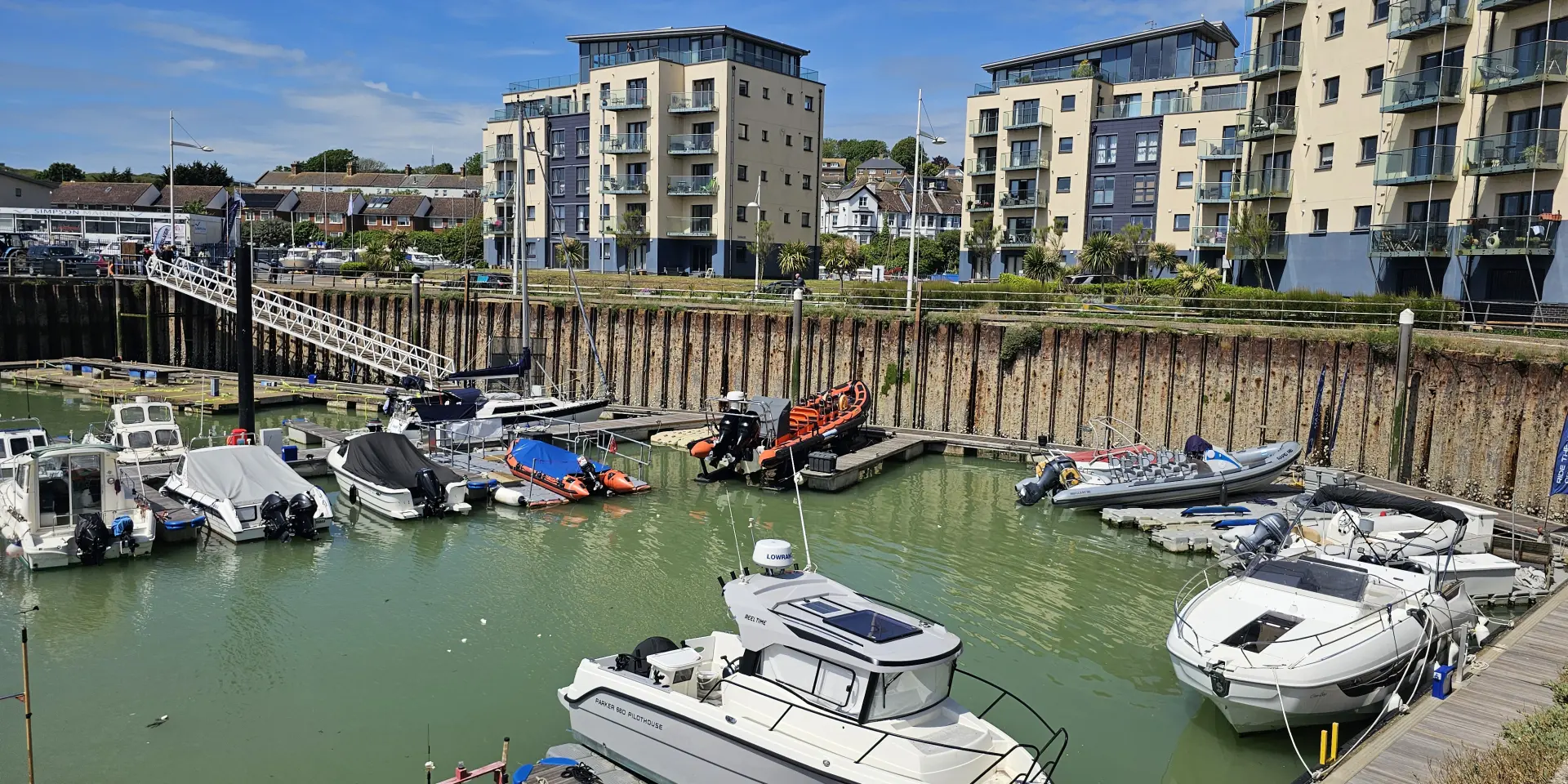 Bateaux de plaisance amarrés dans le port de Newhaven, bordé d’immeubles résidentiels sous un ciel bleu.