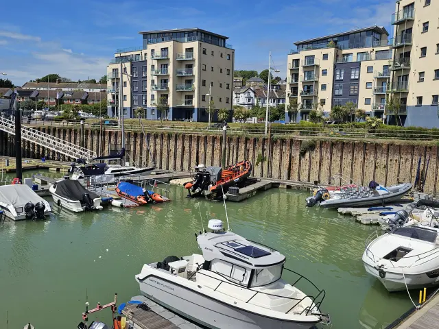 Bateaux de plaisance amarrés dans le port de Newhaven, bordé d’immeubles résidentiels sous un ciel bleu.