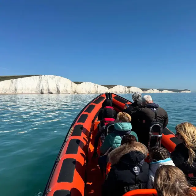 Passagers lors d’une sortie en bateau face aux falaises blanches des Seven Sisters, sur une mer calme sous un ciel dégagé.