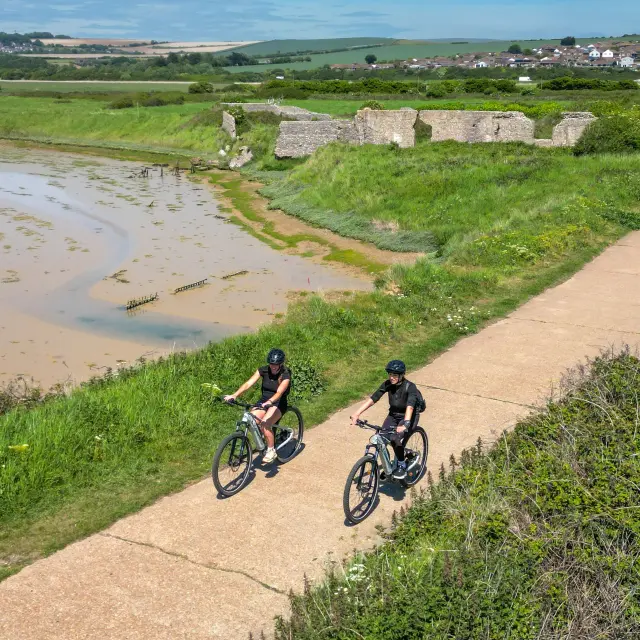 Deux cyclistes parcourent l’Avenue Verte à Newhaven, sur un itinéraire bordé de verdure et de paysages de campagne.