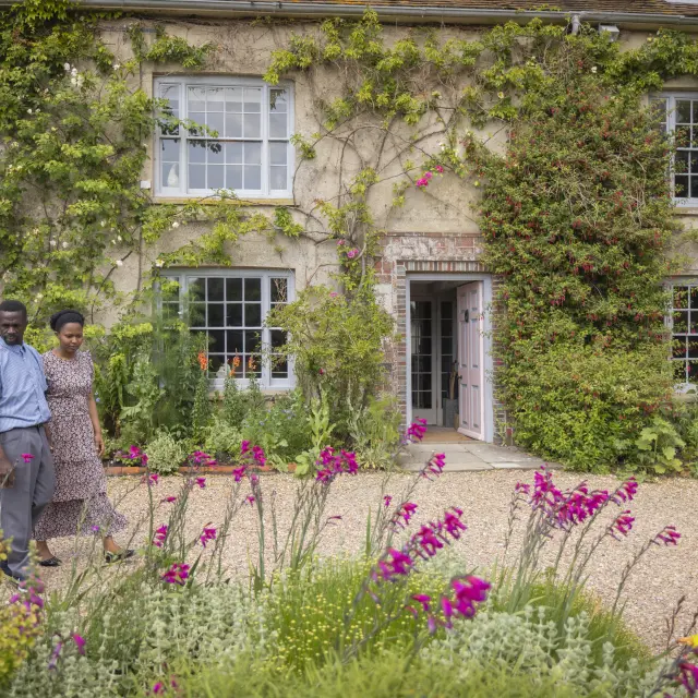 Deux visiteurs se promènent dans le jardin fleuri de Charleston, devant la maison aux murs couverts de plantes grimpantes.