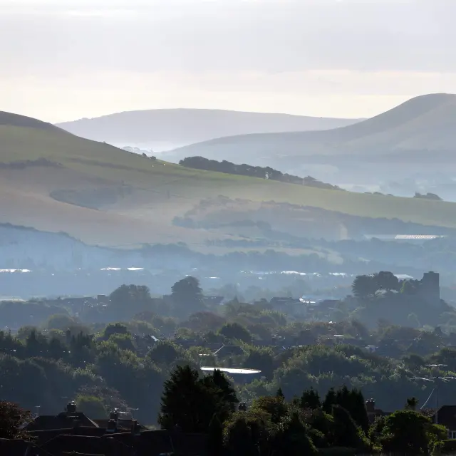 Vue panoramique sur Lewes, dominée par son château et entourée des collines verdoyantes des South Downs dans une légère brume.