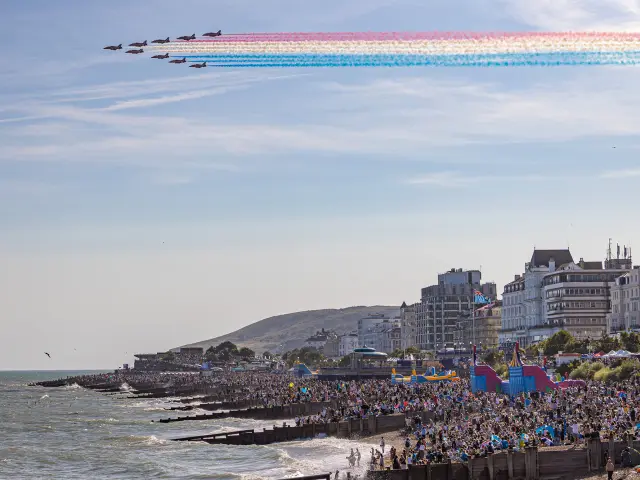 La patrouille des Red Arrows survole le front de mer d’Eastbourne en traçant des fumées rouges, blanches et bleues devant une foule nombreuse.