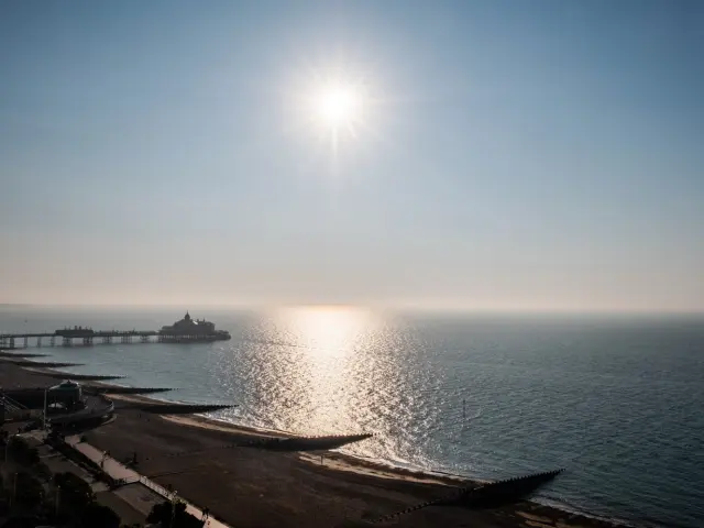 Vue panoramique sur la plage et la jetée d’Eastbourne sous un soleil éclatant, dont la lumière se reflète sur la Manche.
