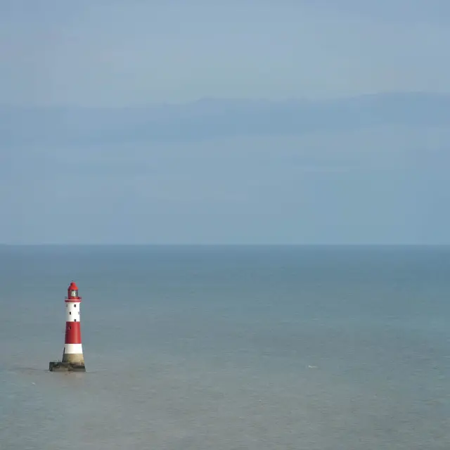Le phare rouge et blanc de Beachy Head se dresse au large dans la Manche, isolé au milieu d’une vaste étendue de mer.