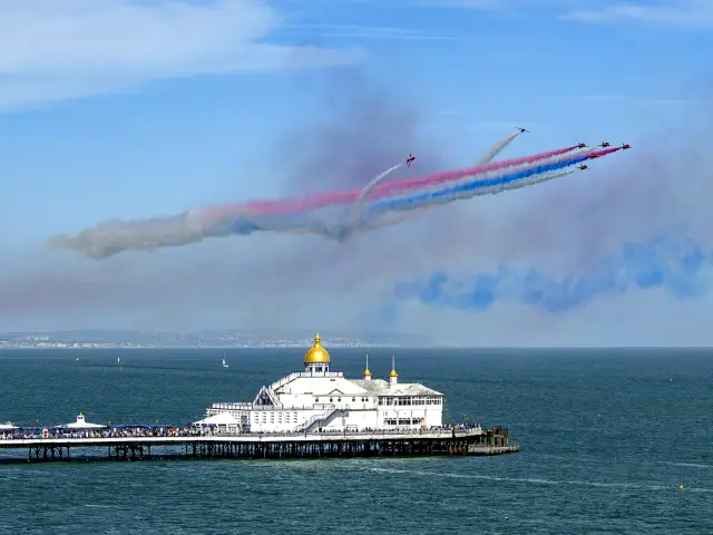 Voltige aérienne au-dessus de l’Eastbourne Pier lors de l’Eastbourne Airshow, avec des traînées de fumée rouges, blanches et bleues.