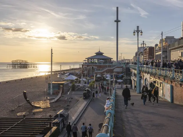 Promeneurs sur le front de mer de Brighton au coucher du soleil, avec la tour Brighton i360 et les vestiges du West Pier au large.
